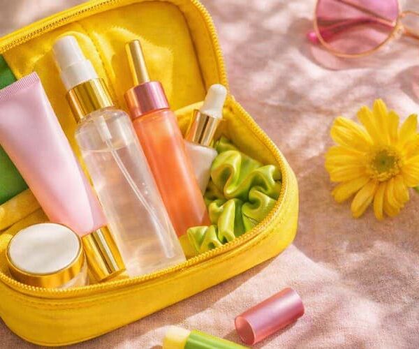 Luxury summer travel beauty flat-lay with skincare essentials in an open cosmetic pouch, including sunscreen, face mist, lip balm and sunglasses in warm natural sunlight