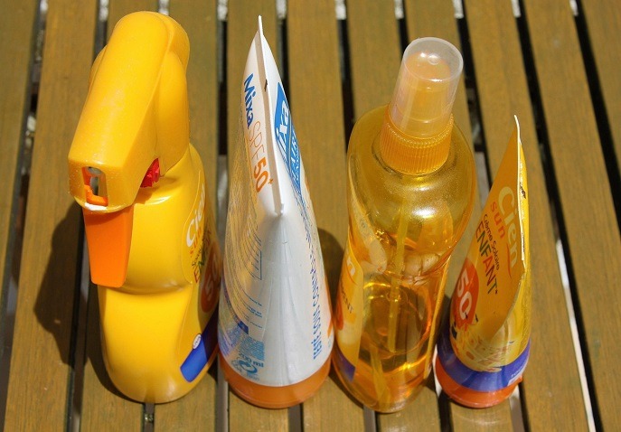 Assorted SPF 50 sunscreen bottles including spray and tube options, with child-friendly formulas, displayed on a wooden surface.