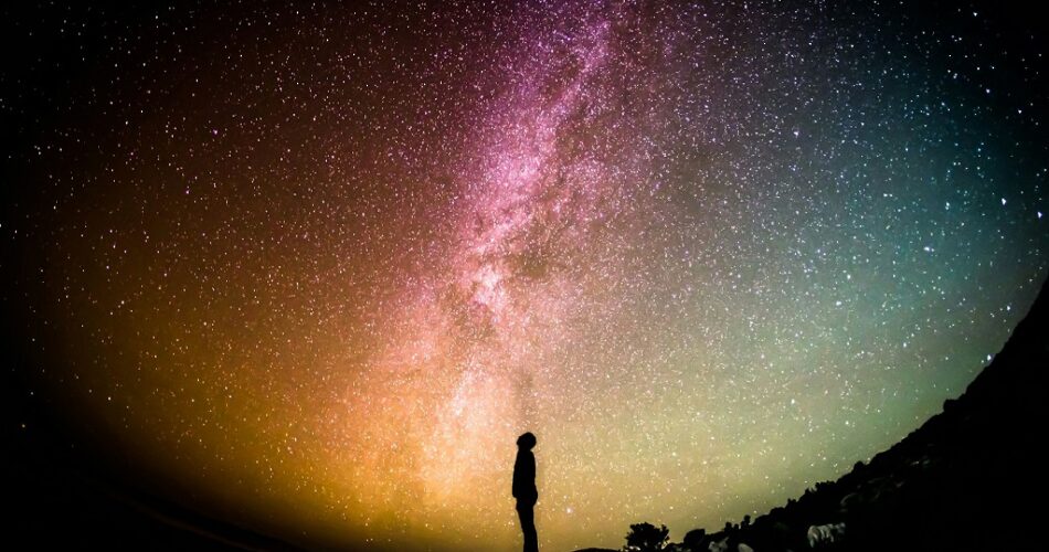 Silhouette of a person stargazing under the vibrant Milky Way with a multicolored night sky.