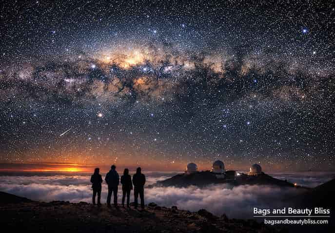 Four people stargazing at Mauna Kea , Hawaii, under the Milky Way with observatory domes above the clouds