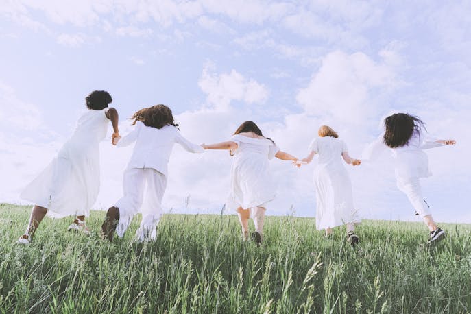A group of women dressed in flowing white outfits joyfully running through Kerala’s lush green fields—symbolizing unity, healing, and the vibrant spirit of sisterhood in nature.
