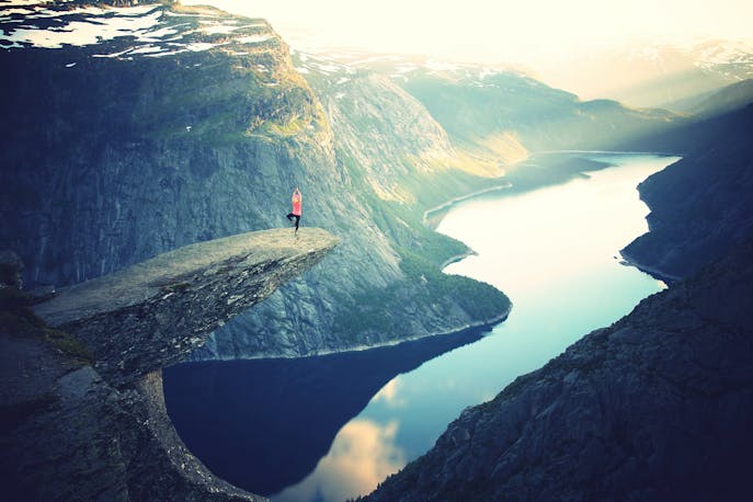 A lone woman standing at the edge of Trolltunga cliff in Norway, overlooking dramatic fjords—capturing a powerful moment of peace, courage, and self-discovery in nature’s grandeur.