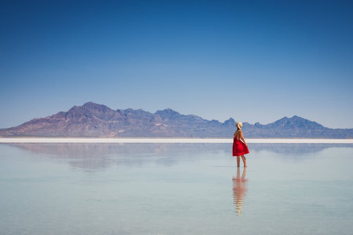Woman in a red dress standing at a distance, surrounded by salt flats and mountains