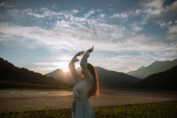 Woman in a pastel shade dress feeling reconnected with herself at a Bali sunrise behind the mountains.