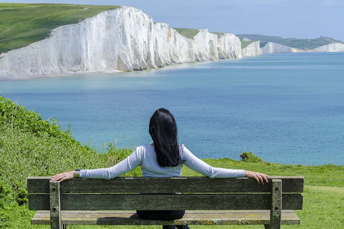 Woman sitting on a bench overlooking mountains and valleys during solo travel