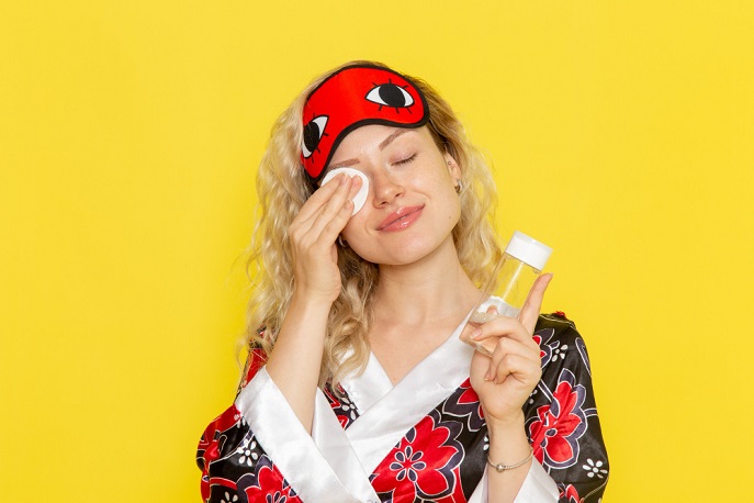 Woman using facial toner with a wipe while having a sleep mask on forehead
