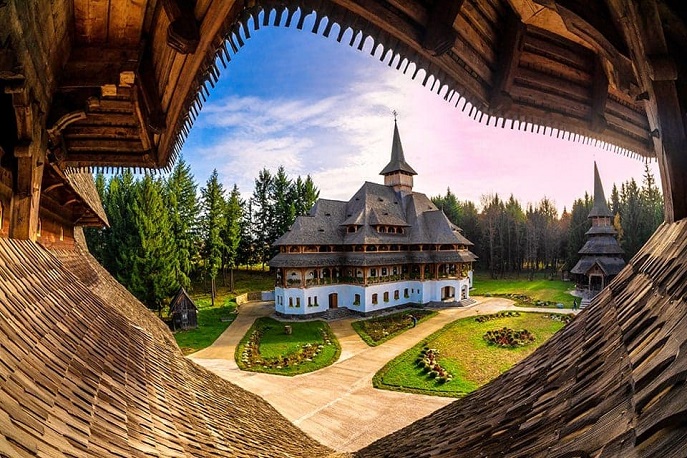 Traditional wooden monastery in Maramureș, Romania surrounded by lush greenery.