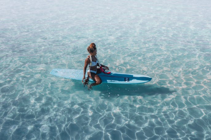 Woman in swimwear sitting on a surfboard in calm turquoise water, reflecting quietly.