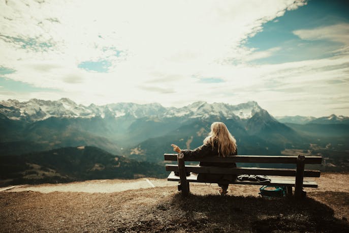 Woman sitting on a bench overlooking mountains and valleys during solo travel in Himachal