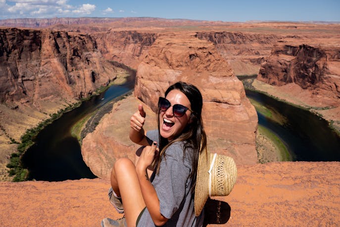 A solo female traveler standing confidently at Horseshoe Bend in Arizona, giving a thumbs up against the backdrop of dramatic red canyons—symbolizing freedom, courage, and the magic of solo adventure.