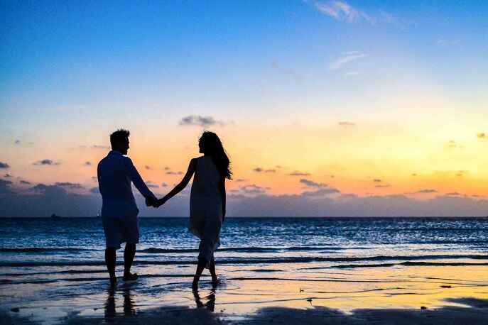 Couple holding hands while walking on the beach during sunrise – safe and romantic travel tips for couples.