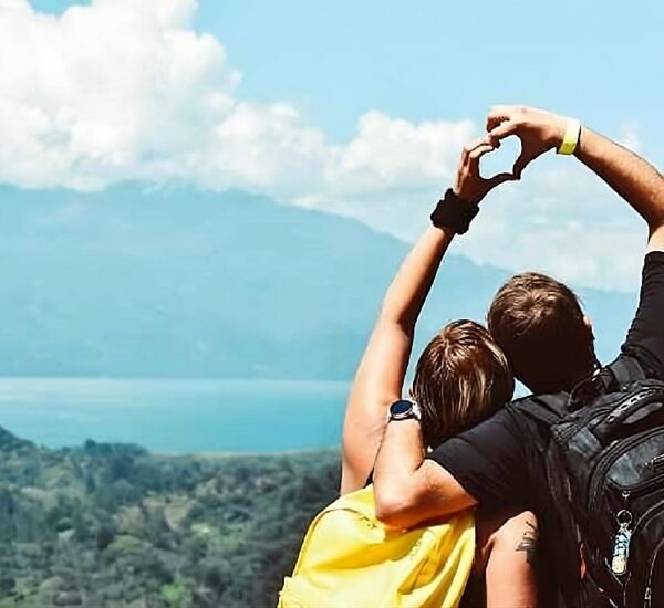 A couple posing a heart with their hands while facing a scenic mountain and cloud.
