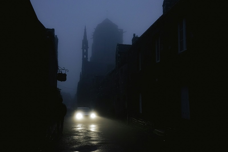 Haunted street with headlights and church silhouette on a rainy Halloween ghost walk USA.