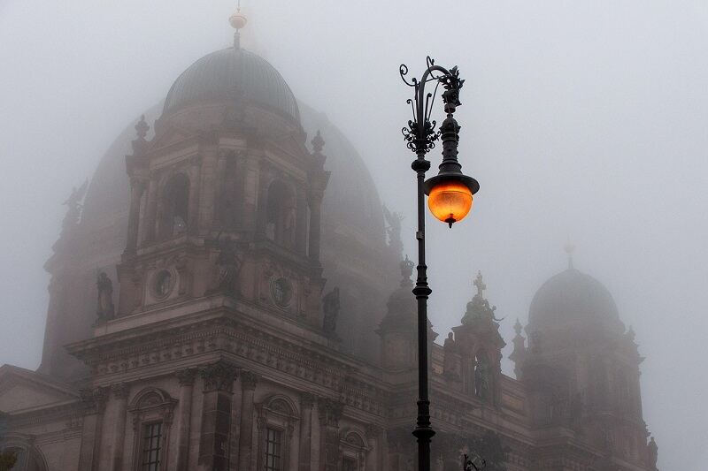 A historic cathedral surrounded by fog with a glowing lamp post on Halloween night.