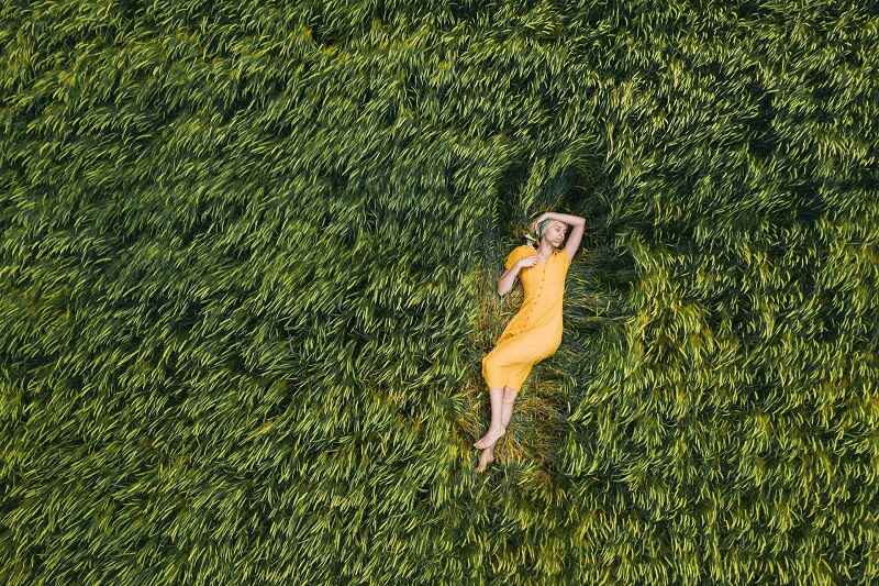 A young woman in yellow dress, laying amidst greenery for wellness