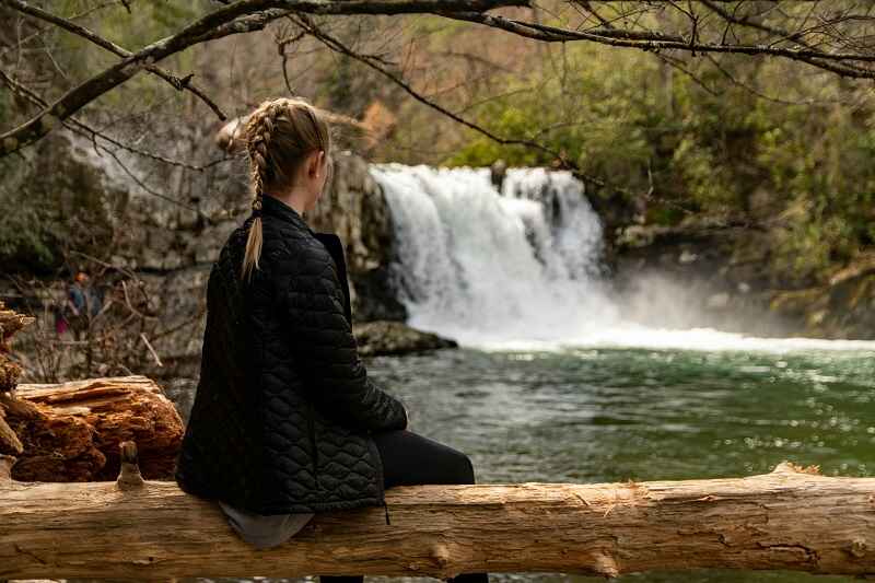 A woman sitting by a waterfall and greenery, relaxing in nature