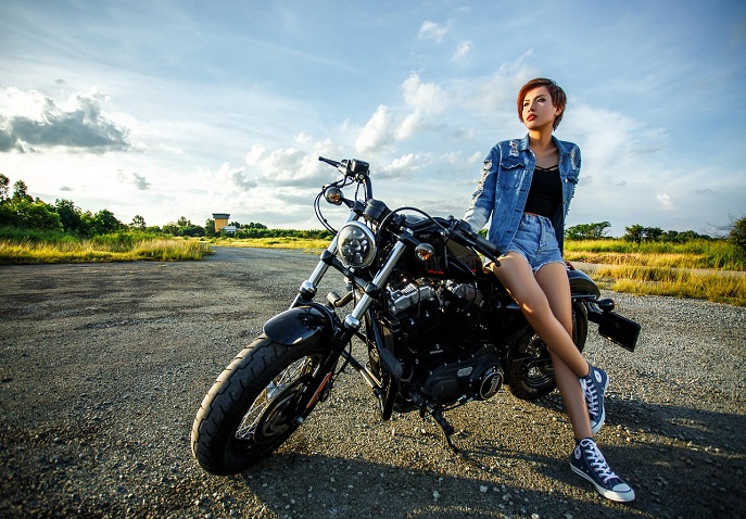  A woman standing by a motorcycle alone on an open road, representing solo travel for women over 40.