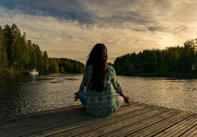 Woman sitting quietly by a lake practising mindfulness during solo travel after 40