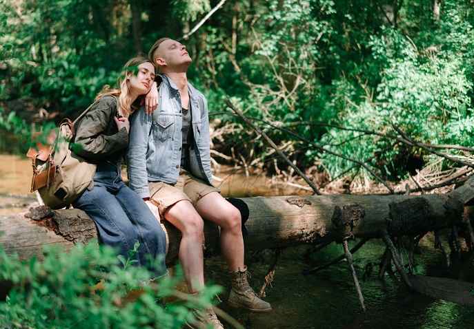 A couple resting on a log in a lush forest during a slow travel Valentine’s Day escape