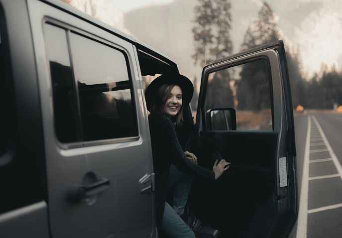 A smiling woman looking from the open car door, showing confidence during a solo trip