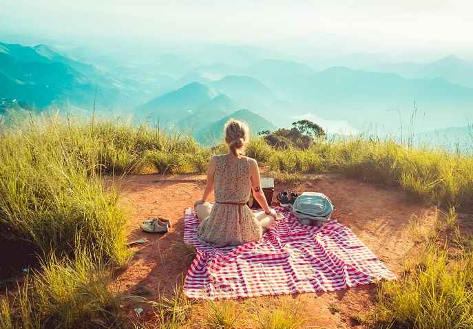 A woman sitting in a hill-surrounded field, practising mindfulness and emotional self-care during a solo trip after 40