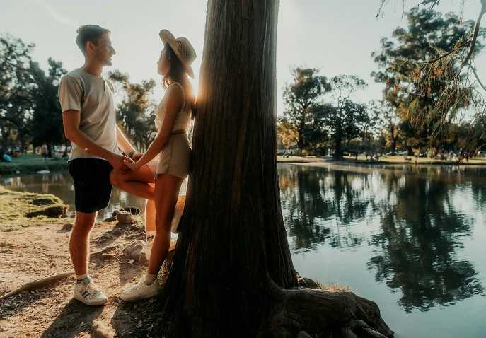 Couple standing by a quiet riverside in a secluded forest, sharing a romantic moment during a wellness retreat for couples