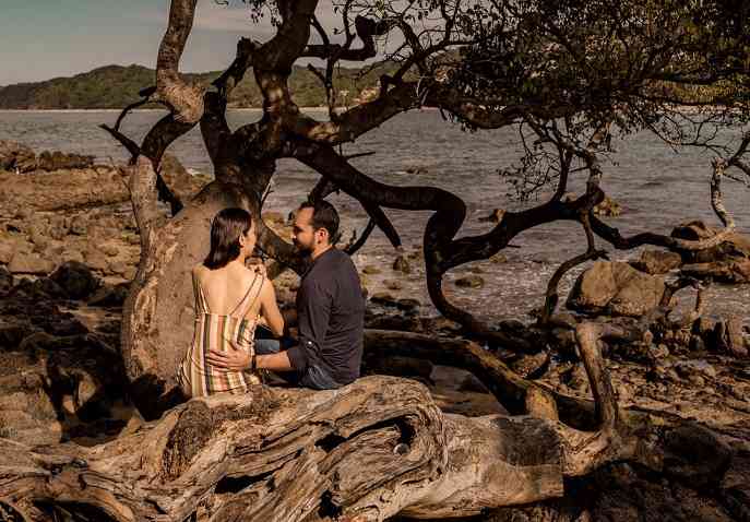 A couple sitting on a dry tree log by the seaside, indulging in some private & peaceful moments.