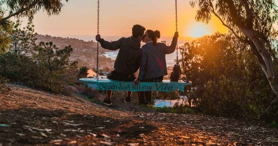 Couple sitting on a swing overlooking a scenic coastal view at sunset