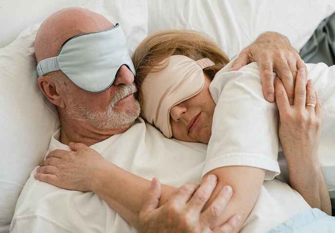 An elderly couple relaxing together with sleeping masks on.